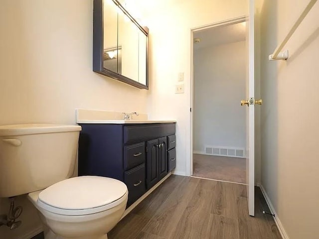 half bathroom featuring toilet, visible vents, wood finished floors, and vanity