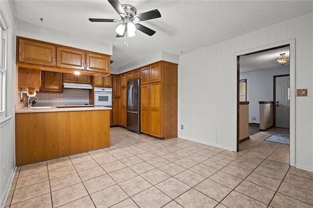 kitchen featuring stainless steel fridge, brown cabinetry, under cabinet range hood, and oven
