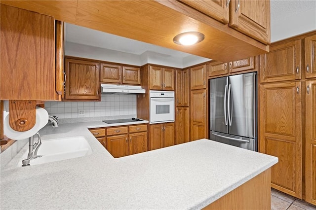 kitchen featuring black electric cooktop, light countertops, freestanding refrigerator, under cabinet range hood, and oven