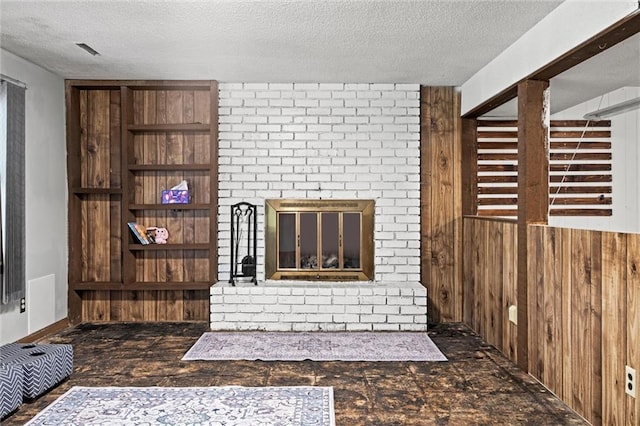 unfurnished living room with a fireplace, wood walls, a textured ceiling, and visible vents