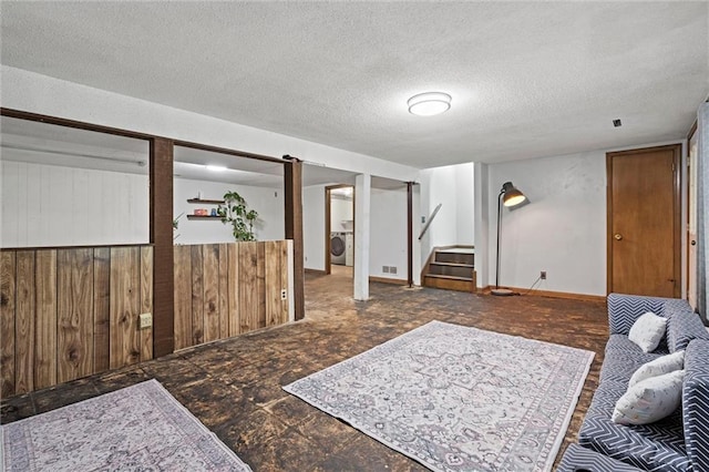 finished basement featuring washer / clothes dryer, a textured ceiling, visible vents, wood walls, and stairway