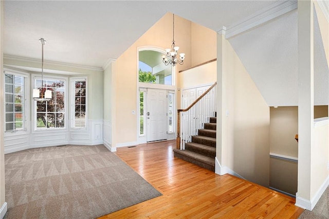 foyer featuring crown molding, wood finished floors, stairway, lofted ceiling, and an inviting chandelier