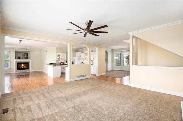 unfurnished living room featuring a ceiling fan, visible vents, ornamental molding, light carpet, and a wealth of natural light