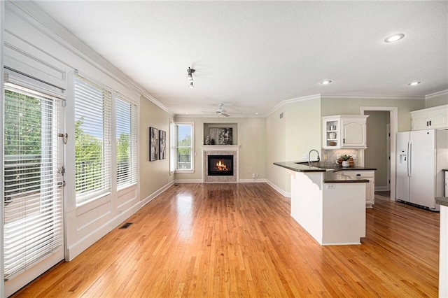 kitchen featuring ceiling fan, dark countertops, white refrigerator with ice dispenser, a peninsula, and light wood-style flooring