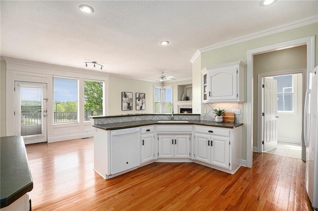 kitchen featuring a peninsula, dark countertops, white appliances, a warm lit fireplace, and a sink