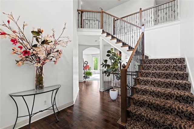 staircase featuring wood finished floors, arched walkways, baseboards, and a towering ceiling