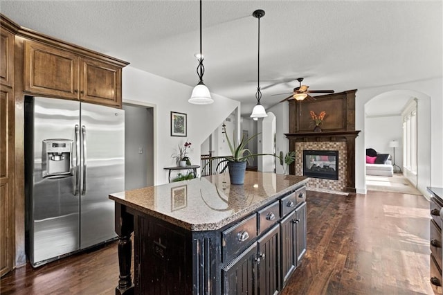kitchen featuring stainless steel refrigerator with ice dispenser, a ceiling fan, light stone countertops, dark wood-type flooring, and a textured ceiling