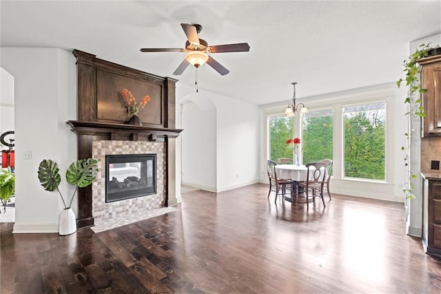 living area with arched walkways, wood finished floors, a brick fireplace, and baseboards