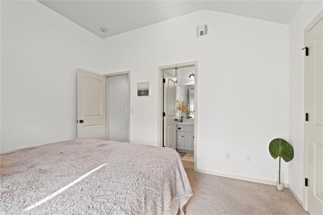 bedroom with light carpet, lofted ceiling, and ensuite bath