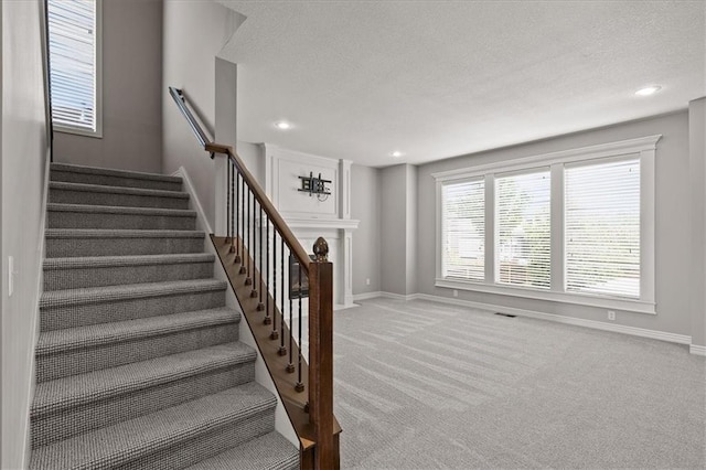 stairway featuring carpet floors, a textured ceiling, baseboards, recessed lighting, and a fireplace with flush hearth