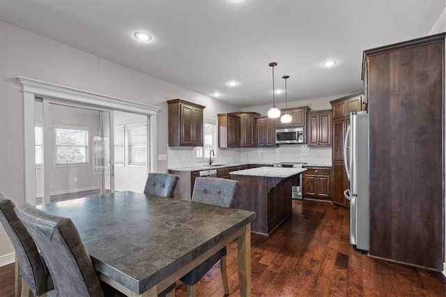 kitchen featuring appliances with stainless steel finishes, a sink, a kitchen island, light countertops, and dark brown cabinets