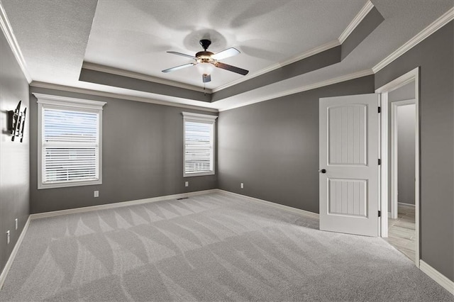spare room featuring a tray ceiling, ornamental molding, carpet flooring, ceiling fan, and plenty of natural light