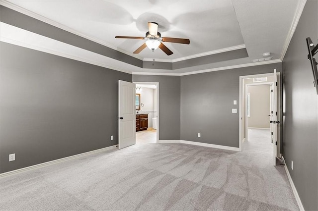 empty room with a raised ceiling, ceiling fan, crown molding, light colored carpet, and baseboards