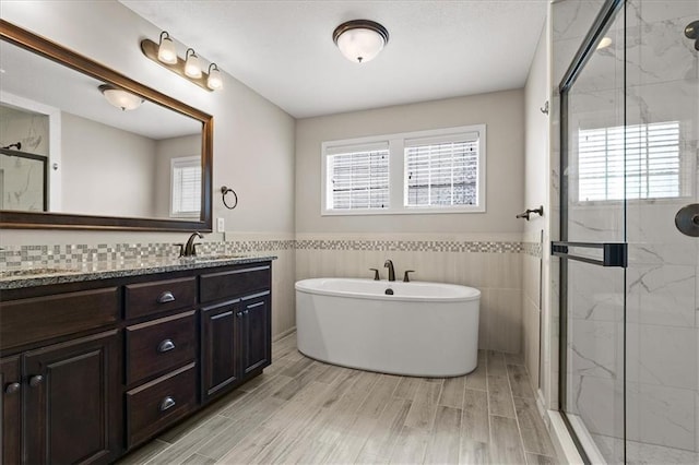 full bathroom with a marble finish shower, tile walls, double vanity, a freestanding tub, and wainscoting