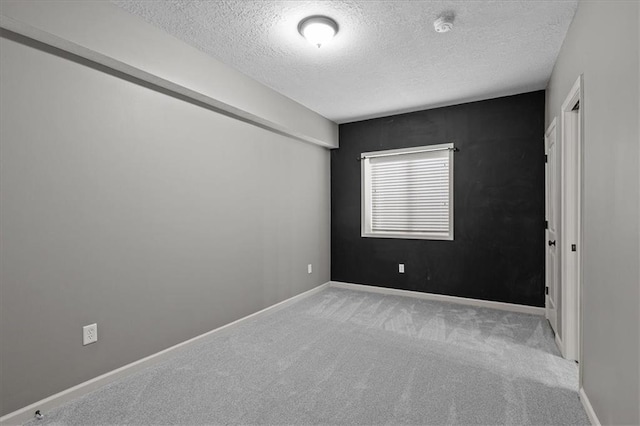 carpeted spare room featuring a textured ceiling, a smoke detector, and baseboards