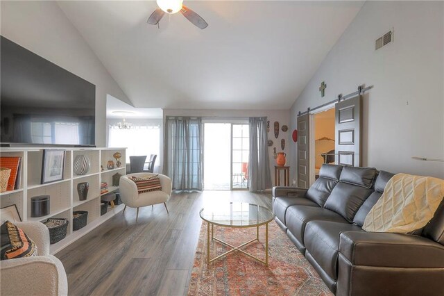 living area with high vaulted ceiling, a barn door, wood finished floors, ceiling fan, and visible vents