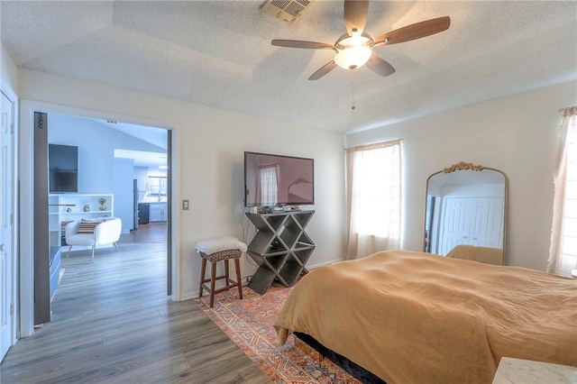 bedroom with a textured ceiling, wood finished floors, visible vents, and baseboards