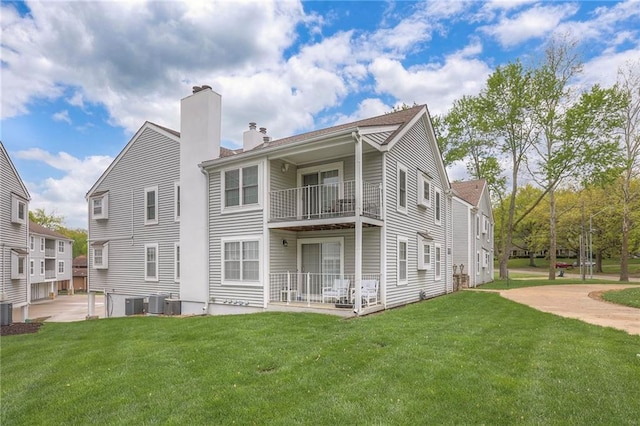 rear view of property featuring a yard, a chimney, and a balcony