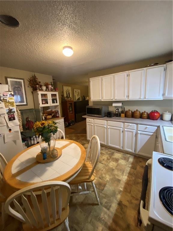 kitchen featuring stainless steel microwave, a textured ceiling, white cabinets, and electric range