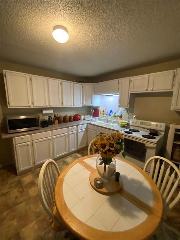 kitchen with a textured ceiling, stainless steel microwave, white cabinets, a sink, and white range with electric cooktop