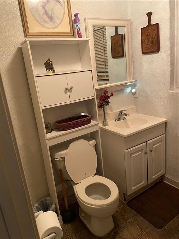 half bath featuring toilet, vanity, a textured wall, and tile patterned floors