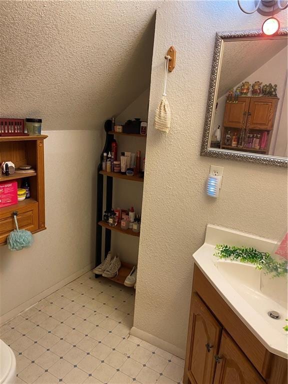 bathroom featuring vanity, tile patterned floors, baseboards, a textured ceiling, and lofted ceiling
