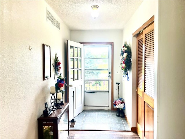 entryway featuring visible vents, a textured ceiling, a textured wall, and baseboards