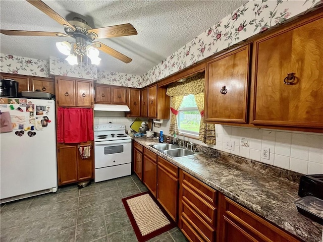 kitchen with a sink, a textured ceiling, white appliances, and wallpapered walls
