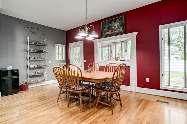 516 Parker St, Osawatomie, KS 66064 - dining room featuring an accent wall, light wood finished floors, a chandelier, baseboards, and plenty of natural light