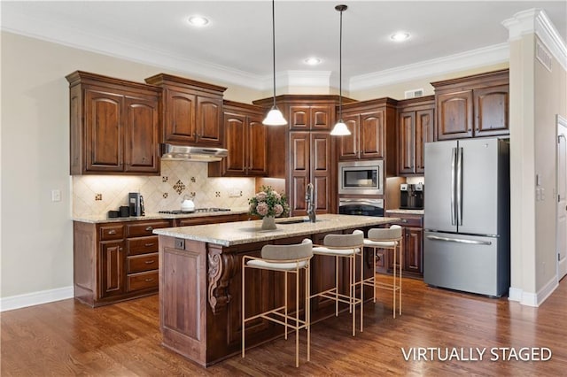 kitchen with stainless steel appliances, under cabinet range hood, dark wood-type flooring, an island with sink, and a breakfast bar