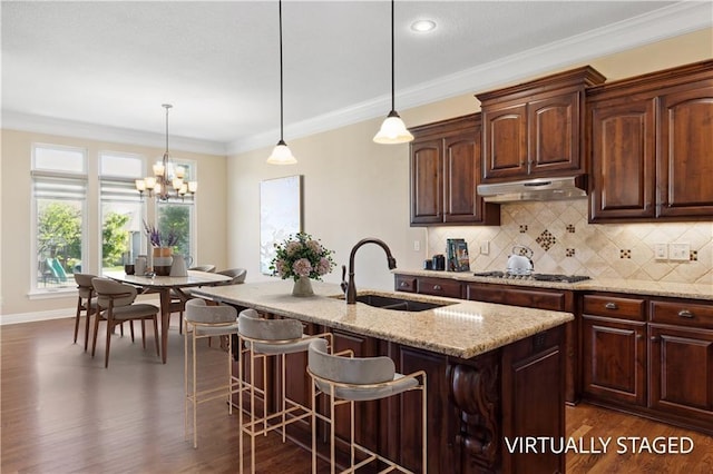 kitchen with under cabinet range hood, a sink, dark wood-style floors, backsplash, and ornamental molding