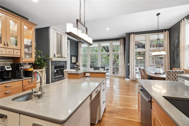 kitchen featuring open floor plan, light wood-type flooring, a large fireplace, a sink, and dishwasher