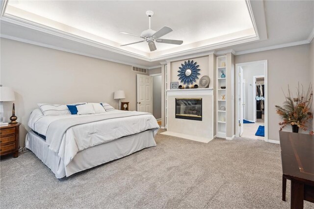 bedroom with crown molding, visible vents, a fireplace with flush hearth, a raised ceiling, and carpet flooring