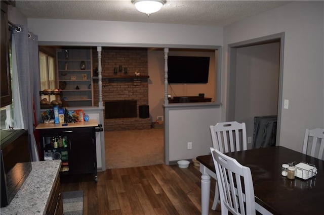 dining room with dark wood-type flooring, a textured ceiling, and a brick fireplace