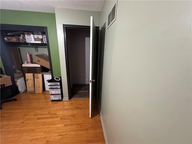 hall featuring baseboards, visible vents, a textured ceiling, and light wood-style flooring