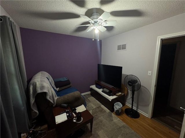 living room featuring visible vents, wood finished floors, ceiling fan, and a textured ceiling