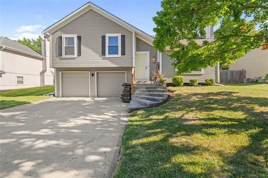 bi-level home featuring fence, concrete driveway, a front lawn, and a garage