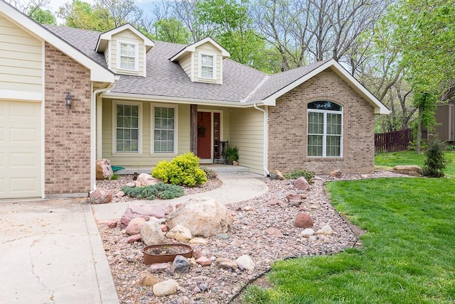 view of front of property with roof with shingles, fence, brick siding, a front yard, and driveway