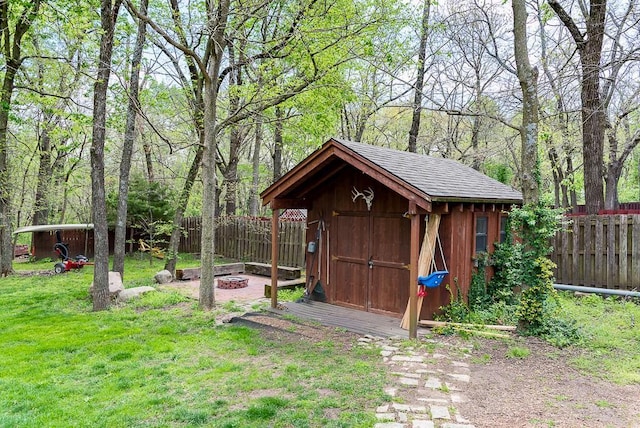 view of shed with a fenced backyard, an outdoor fire pit, and a wooded view