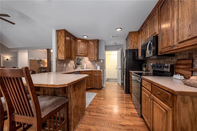 kitchen featuring ceiling fan, electric range oven, a breakfast bar area, a peninsula, and stainless steel microwave