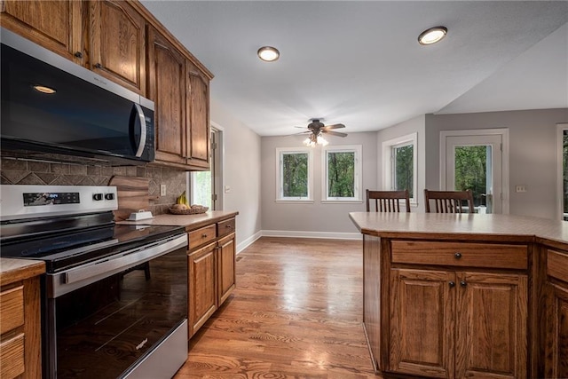 kitchen with backsplash, appliances with stainless steel finishes, light countertops, baseboards, and light wood-style floors