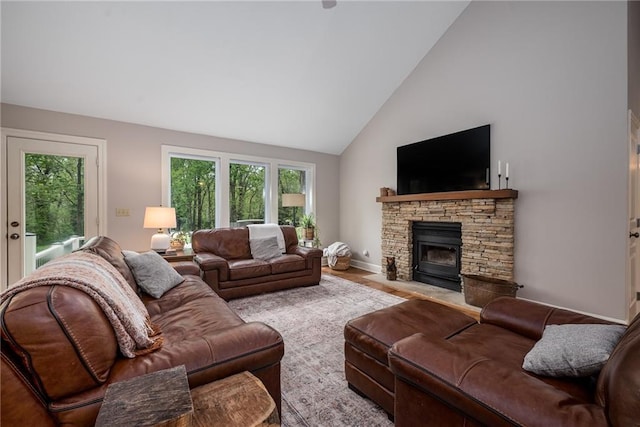 living area featuring a stone fireplace, baseboards, a wealth of natural light, and high vaulted ceiling