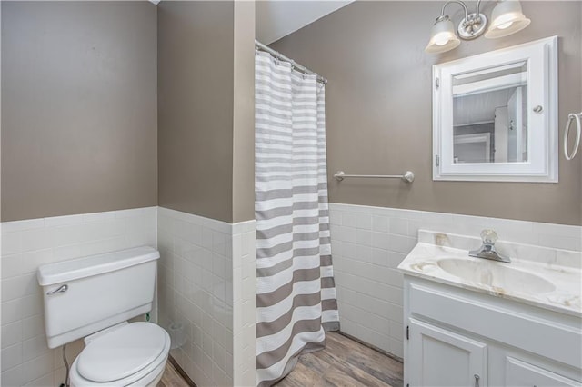 306 S 5th St, Neodesha, KS 66757 - full bath featuring wood finished floors, tile walls, a wainscoted wall, toilet, and vanity