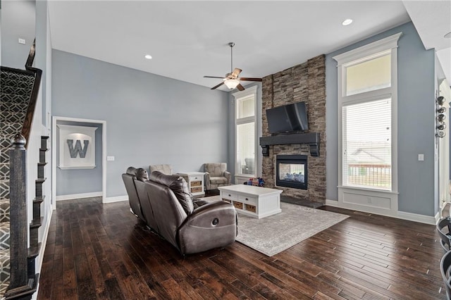 living area featuring wood-type flooring, a ceiling fan, baseboards, and a stone fireplace