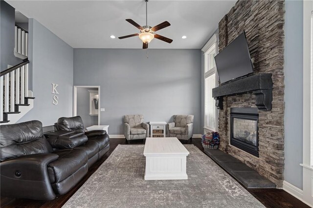 living area with ceiling fan, a fireplace, wood finished floors, baseboards, and stairs