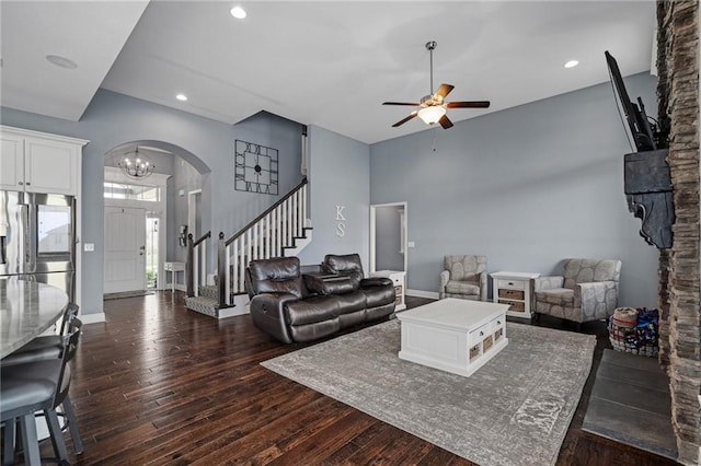 living room with arched walkways, stairway, ceiling fan with notable chandelier, recessed lighting, and dark wood-type flooring