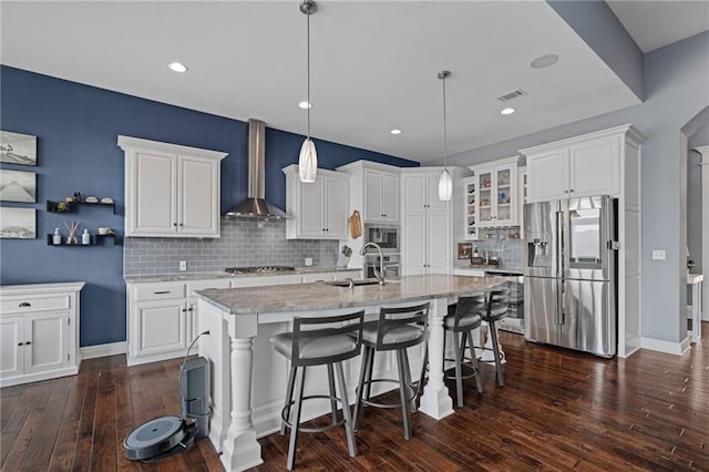 kitchen with backsplash, visible vents, a sink, stainless steel appliances, and wall chimney exhaust hood