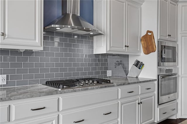 kitchen featuring wall chimney range hood, white cabinetry, appliances with stainless steel finishes, and tasteful backsplash