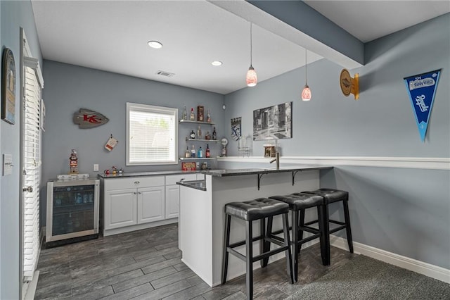 kitchen featuring a breakfast bar, beverage cooler, white cabinetry, decorative light fixtures, and visible vents