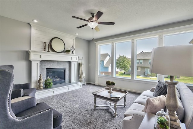 carpeted living room featuring a fireplace, a textured ceiling, a ceiling fan, and baseboards